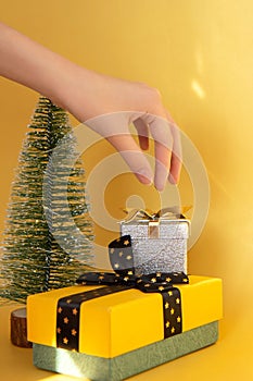 Two gift boxes, Christmas tree and a woman& x27;s hand on bright gold background
