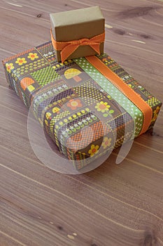 Two gifts in vintage wrapping paper with flowers and mushrooms, green brown and orange, neutral wood background