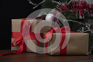 Two gifts wrapped in craft paper with a red wide ribbon stand on a wooden table with a black background. Holidays