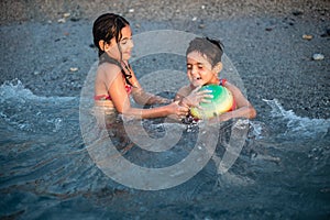 two gils in swimsuits playing with colourful ball in the sea waves