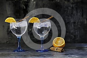 Two gin tonics on blue glass with cinnamon and orange