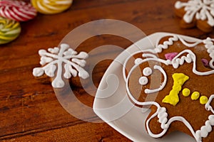 Two gingerbread men with colorful icing on a white dessert plate on a wooden table with gingerbread and caramels in the background