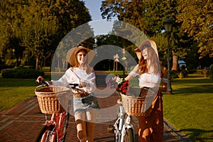 Two girl best friends nice conversation while walking with bicycle at park