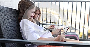 Two girl child sisters are sitting in patio and having fun with tablet