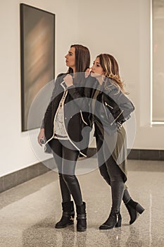 Two girl friends looking at modern painting in art gallery