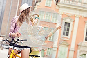 Two girl friends using map while riding tandem bicycle