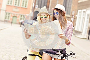 Two girl friends using map while riding tandem bicycle
