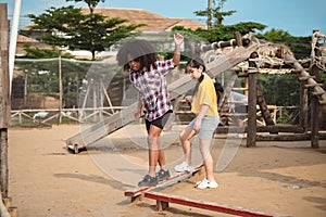 Two girl kid walks on a log, keeping her balance, walking on the playground