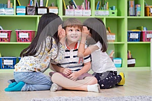 Two girl kids whisper secret at ear of boy in library at kindergarten preschool,Fun and happy children,back to school concept photo