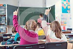 Two girl students raising hands to answer a question in school class