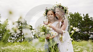 Two girl teenager in floral wreath with flowers bouquet standing on blooming field. Romantic girls with flower bouquet