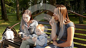 Two girlfriends with a child sit on a bench in the city Park and eat ice cream. Homosexual couple, young lesbian women