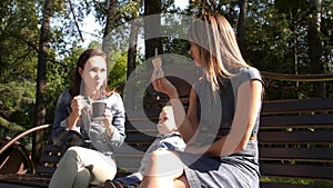 Two girlfriends with a child sit on a bench in the city Park and eat ice cream. Homosexual couple, young lesbian women