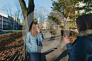 Two girlfriends drink morning coffee talk standing park