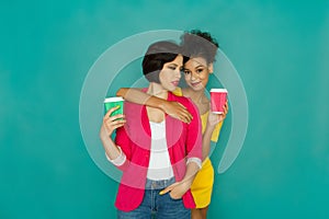 Two girlfriends drinking coffee at turquoise studio background