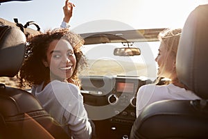 Two girlfriends driving with sunroof open, one turning round