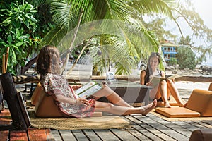 Two girlfriends enjoying tropical vacation sitting in bamboo beach bar