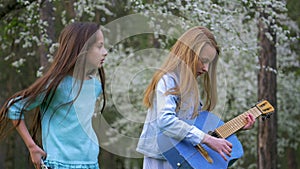 Two girlfriends having fun outdoors. Young people enjoying a spring day in forest. small girls playing guitar sing songs.