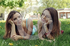 Two girlfriends lie on a green lawn