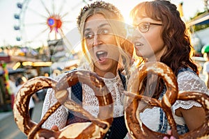 Two girlfriends look amazed with pretzel or brezen on a Bavarian fair or oktoberfest or duld in national costume or Dirndl