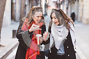 Two girlfriends looking into a coffee cup with shocked faces