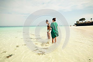 Two girlfriends on the ocean considering starfishes on sunny day