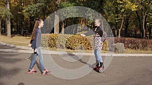 Two girlfriends riding on an electronic scooter in an autumn park
