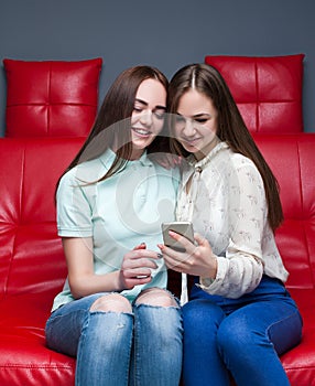 Two girlfriends secretive on red leather couch