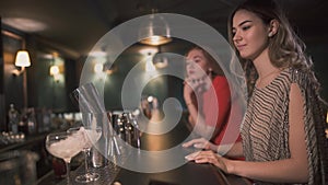 Two girlfriends sitting at bar counter waiting when bartender will make them cocktails. Leisure of beautiful girls