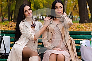 Two girlfriends sitting on bench with shopping