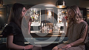 Two girlfriends sitting near bar counter having interesting conversation close up. Women drinking cocktails. Leisure of