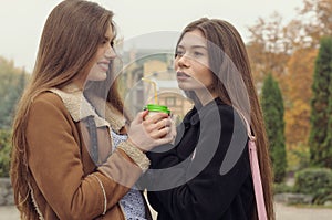 Two girlfriends try to warm up with a hot drink in the outdoors