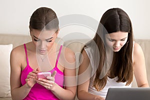 Two girlfriends using mobile phone and laptop
