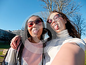 two beautiful young girls making funny faces  wearing sunglasses and casual clothes  outdoors