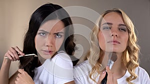 Two girls applying make up, fighting for place in front of mirror, rivalry, envy