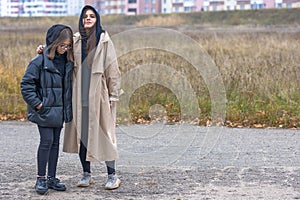 Two girls in autumn clothes stand together on a deserted outskirts of the city