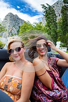 Two girls at the back seat of a convertible car.