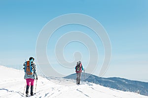 two girls with backpacks walk along a path in the winter mountains. hiking in the mountains