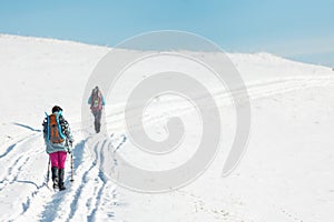 two girls with backpacks walk along a path in the winter mountains. hiking in the mountains