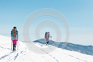 two girls with backpacks walk along a path in the winter mountains. hiking in the mountains