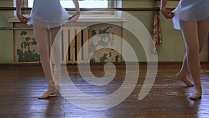 Two girls in ballet shoes do exercises during ballet class in frayed classroom