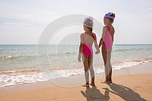 Two girls in bathing suits standing on beach and look at the horizon