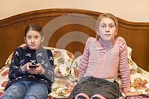 Two girls in bed are watching TV. Cute little girls sitting on a bed together watching television. The concept of children`s