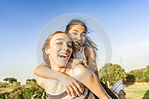 Two girls best friends having fun outdoor in a green nature park looking at camera laughing and joking. Young brunette woman