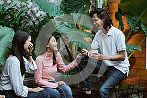 two girls and a boy are laughing cheerfully in the garden holding cups