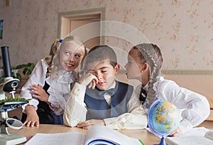 Two girls and a boy at school at a Desk studying biology and geography, discussing homework