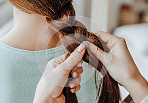 Two girls braid their hair at the window. Woman makes a braid to her friend. Hair weaving hairstyles. Girlfriend braids her hands