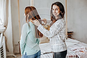 Two girls braid their hair at the window. Woman makes a braid to her friend. Hair weaving hairstyles. Girlfriend braids her hands