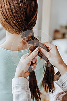 Two girls braid their hair at the window. Woman makes a braid to her friend. Hair weaving hairstyles. Girlfriend braids her hands