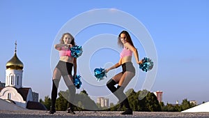 Two girls cheerleaders with pompons dancing outdoors